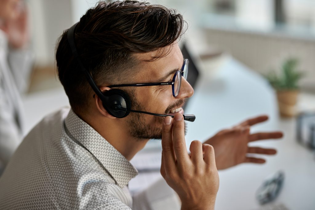 Happy call center agent wearing headset while talking with clients and working in the office.